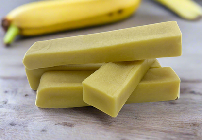 Image of four yellow banana yak sticks stacked and on a light wood surface