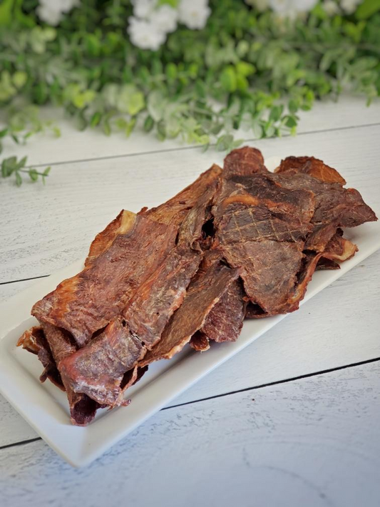 Image of bison treat pieces on a white plate with greenery in the background 