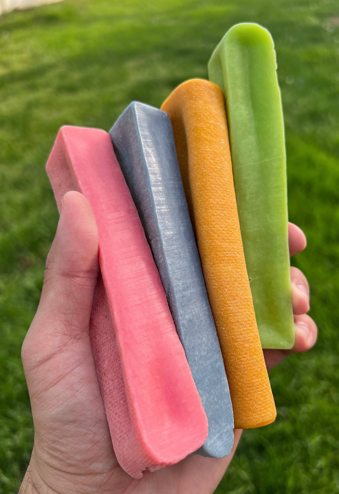 Image of a hand holding an orange, blue, green and pink yak cheese with grass in the background