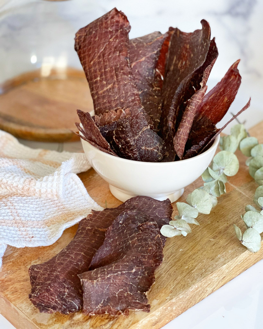 Image of multiple angus beef pieces in a white bowl and on a wood cutting board. 