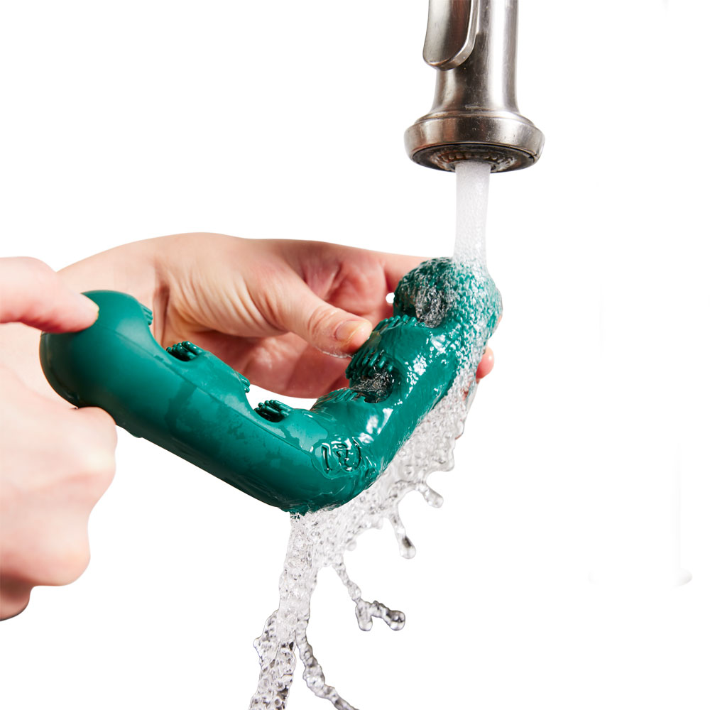 a green “v” shaped treat holder being ran under running water